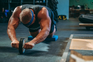 Male athlete doing ab wheel rollouts.