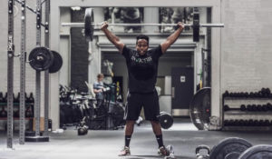 Male athlete holds a barbell overhead in an empty gym.