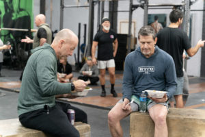 Group of masters athletes eating lunch on boxes in the gym.