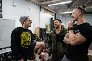 Group of athletes discuss workout strategy with their coach who is fashioning a stylish beanie and fancy glasses.