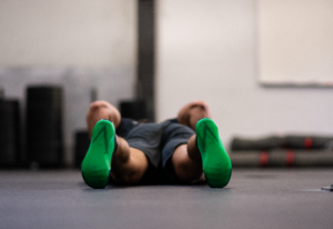 Athlete in the bottom of a burpee with the soles of his shoes showing off the Invictus "V".