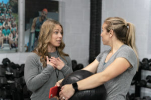 A coach gives tips to an athlete who is holding a medicine ball.