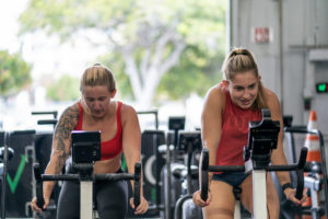 Two female athletes on exercise bikes having a great Zone 2 workout sesh.