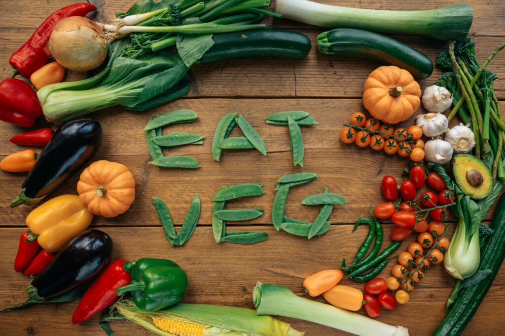 Colorful veggies on a cutting board surrounding "eat veg" spelled out in sweet peas.