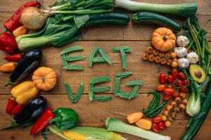 Colorful veggies on a cutting board surrounding "eat veg" spelled out in sweet peas.