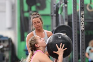 A coach watching over her athlete as she does wall balls.